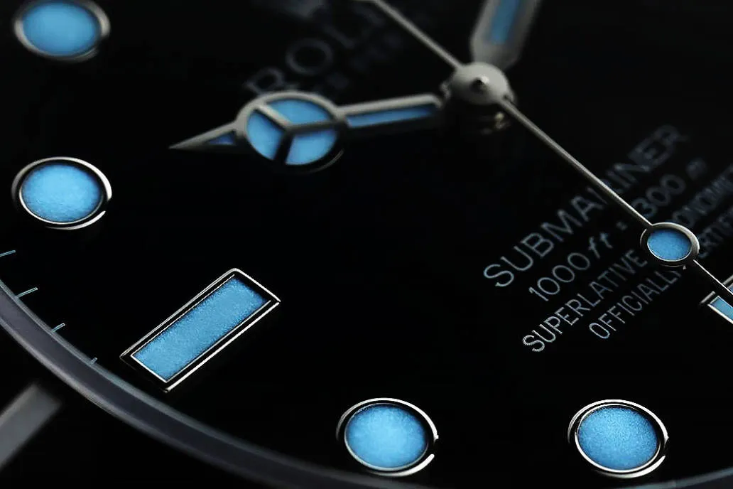 Close-up of glowing Rolex Submariner replica dial in darkness, featuring blue Super-Luminova lume on markers and hands for clear nighttime use.